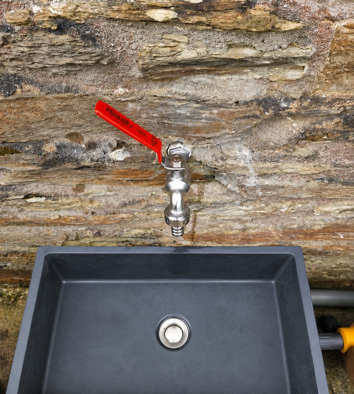 Outside tap with red lever fitted to stone wall above a Belfast-style sink